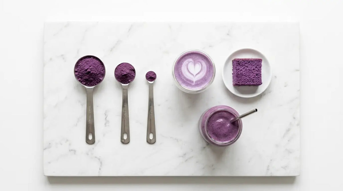 Trois cuillères doseuses de poudre d'ube violette en tailles décroissantes, à côté d'un latte, d'un gâteau et d'un smoothie